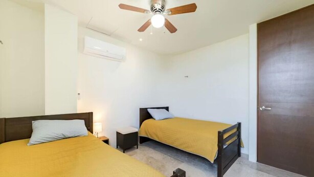 A room with two beds, a ceiling fan, an air conditioning unit, and a door. - Beachfront Paradise with Shared Pool Telchac | Depto A12 (Telchac Puerto)