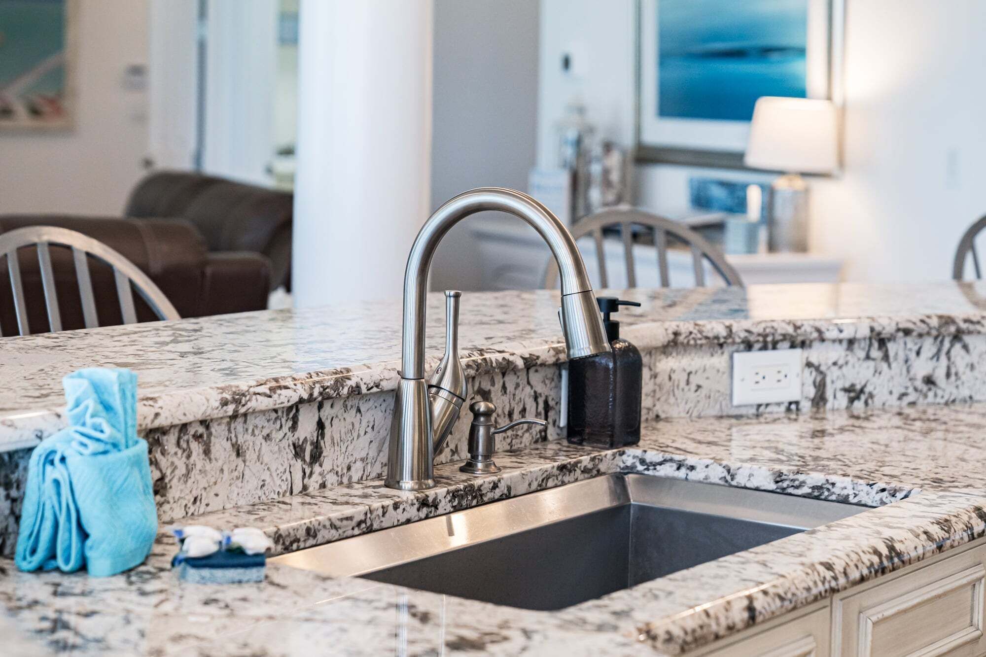 A kitchen with a granite countertop, stainless steel sink, and a soap dispenser.