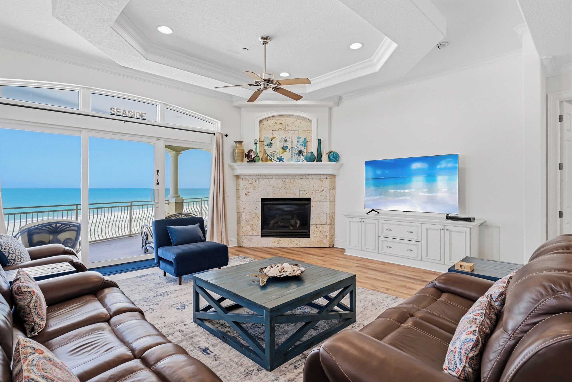 Uma sala de estar ampla com sofás de couro, lareira, televisão e varanda com vista para o mar.