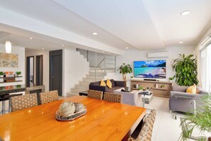 A modern living room with a wooden dining table, sofas, a TV, and a staircase. - 4-bedroom house with private pool in a safe community with 24/7 security (cancun)
