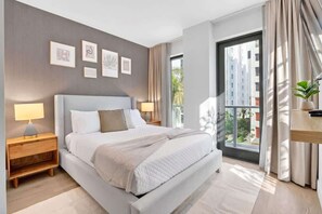 A modern hotel room with a large bed, bedside tables, a view of the city, and artwork on the wall. - Modern Studio with Balcony, Pool & Gym Access (Miami)
