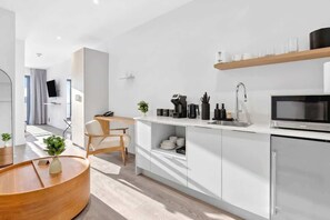 A modern kitchen with a microwave, coffee maker, and a shelf with cups. - Modern Studio with Balcony, Pool & Gym Access (Miami)