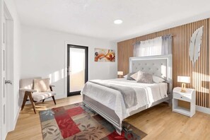 A bedroom with a bed, bedside tables, a chair, a door, and a wall with vertical lines and a feather decoration. - 4BR Oasis Near MIA - Jacuzzi - Games - BBQ (Miami)