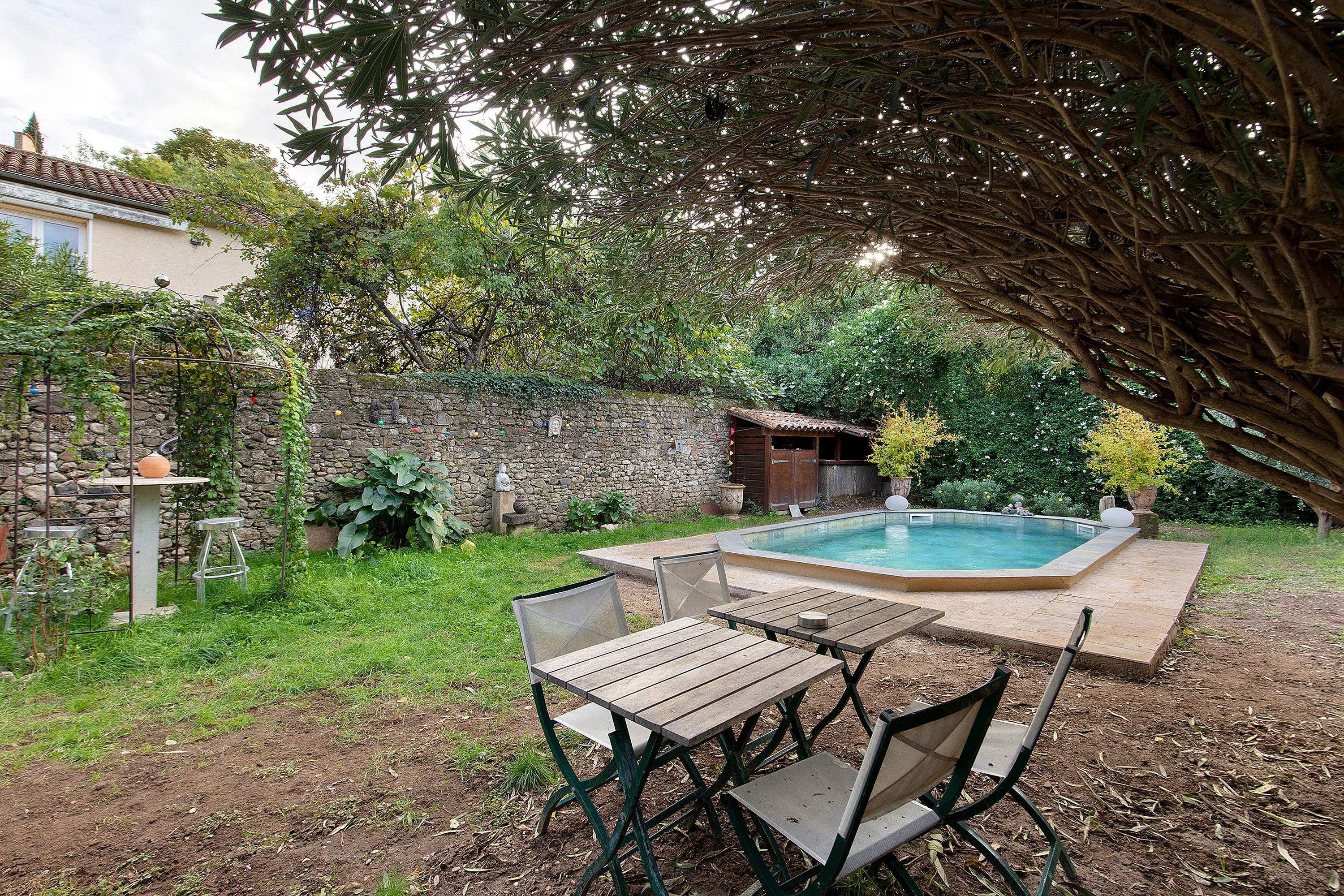 A backyard with a swimming pool, a stone wall, and a wooden table with chairs.