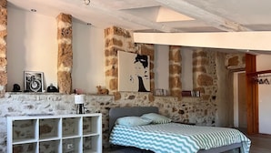 A bedroom with a stone wall, a bed with striped bedding, a white console table, and a mounted artwork. - Gîtes de la Soulondre: Vacation Home with Mountain View, Shared Pool, and Wi-Fi (Lodève)