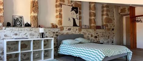 Ein Schlafzimmer mit Steinwand, einem Bett mit gestreifter Bettwäsche, einem weißen Konsolentisch und einem aufgehängten Kunstwerk.
