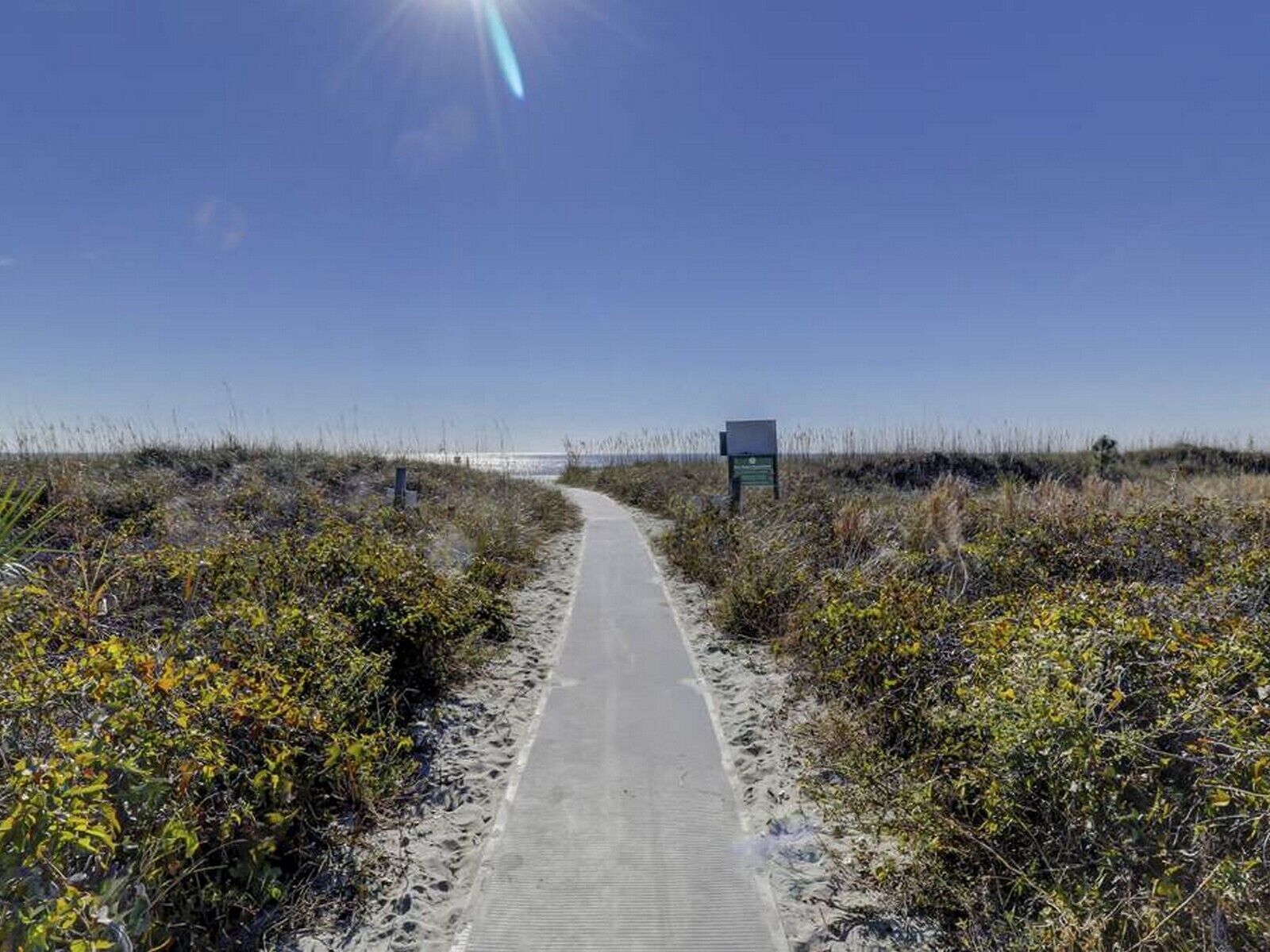 A pathway leading to a beach with a signboard in the distance.