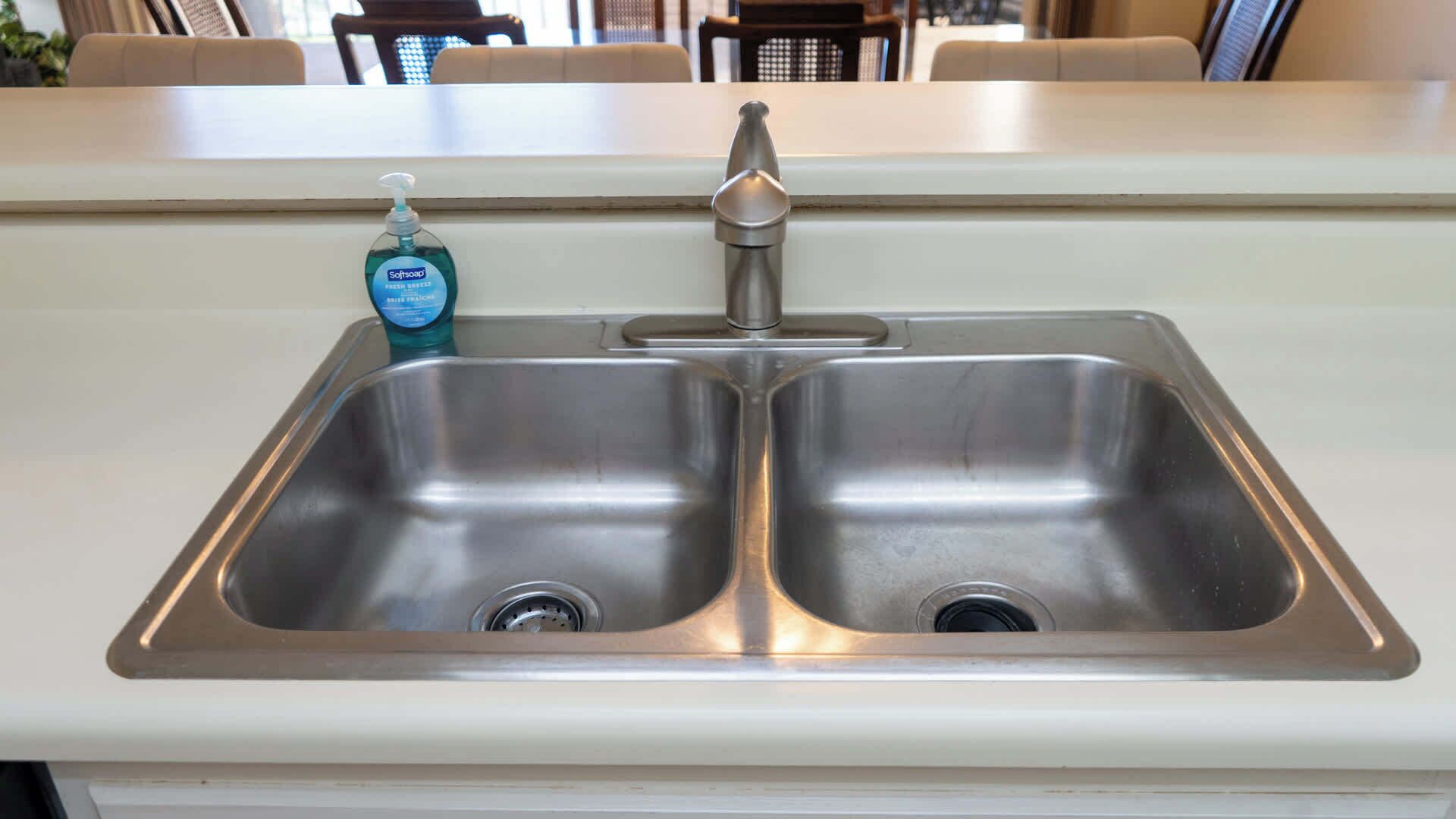 A stainless steel kitchen sink with a faucet and a bottle of soft soap.