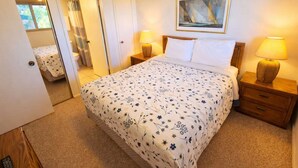 A bedroom with a bed, two bedside tables with lamps, a painting on the wall, and a door leading to another room. - 2BR Half Block to Beach, Pool Hot Tub Patio SPI (South Padre Island)
