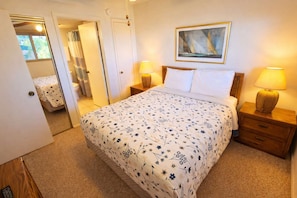 A bedroom with a bed, two bedside tables with lamps, a painting on the wall, and a door leading to another room. - 2BR Half Block to Beach, Pool Hot Tub Patio SPI (South Padre Island)