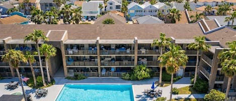 Et hotel med flere etager, en pool, udendørs siddepladser og palmer.