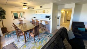 A dining area with a glass-top table and chairs, a ceiling fan, and a kitchen area with a microwave and cabinets. - 2BR Half Block to Beach, Pool Hot Tub Patio SPI (South Padre Island)