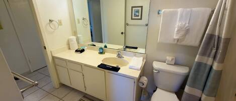A bathroom with a sink, mirror, toilet, and shower curtain.