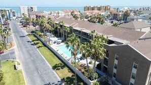 A hotel with a swimming pool, palm trees, and a view of the ocean. - 2BR Half Block to Beach, Pool Hot Tub Patio SPI (South Padre Island)
