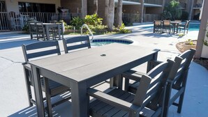 A patio area with a pool, outdoor seating, and a building in the background. - 2BR Half Block to Beach, Pool Hot Tub Patio SPI (South Padre Island)