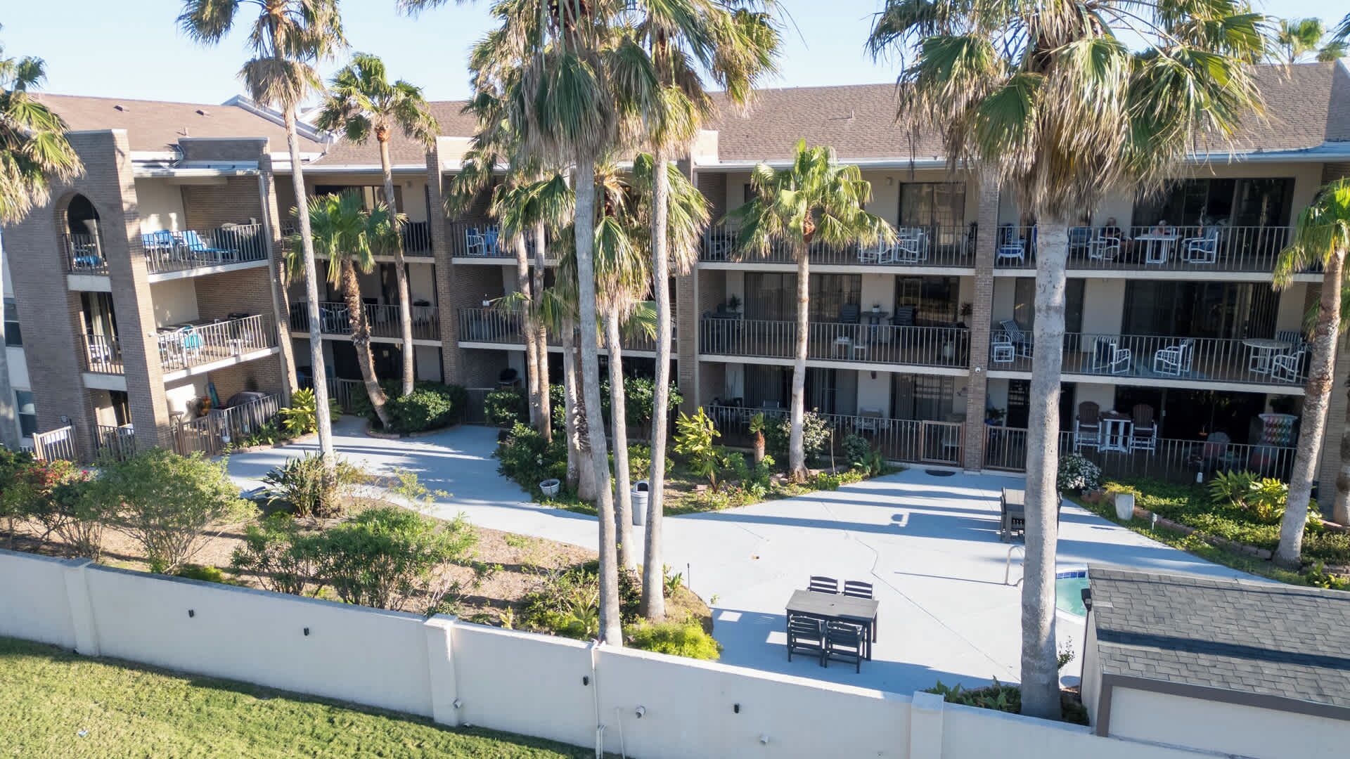 A multi-story hotel with balconies, palm trees, and outdoor seating areas.