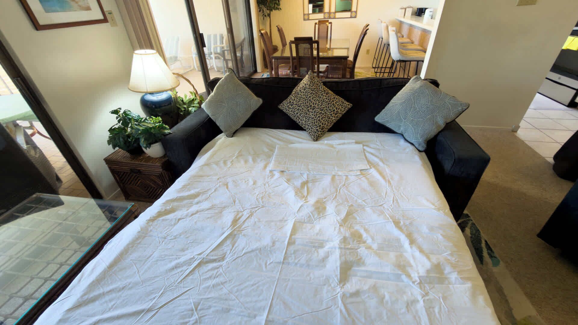 A bed with white bedding, two pillows, a nightstand with a lamp, and a potted plant.