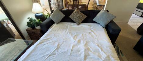 A bed with white bedding, two pillows, a nightstand with a lamp, and a potted plant.