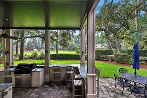 Une terrasse extérieure couverte, équipée d’un barbecue, de sièges et offrant une vue sur un jardin bien entretenu.
