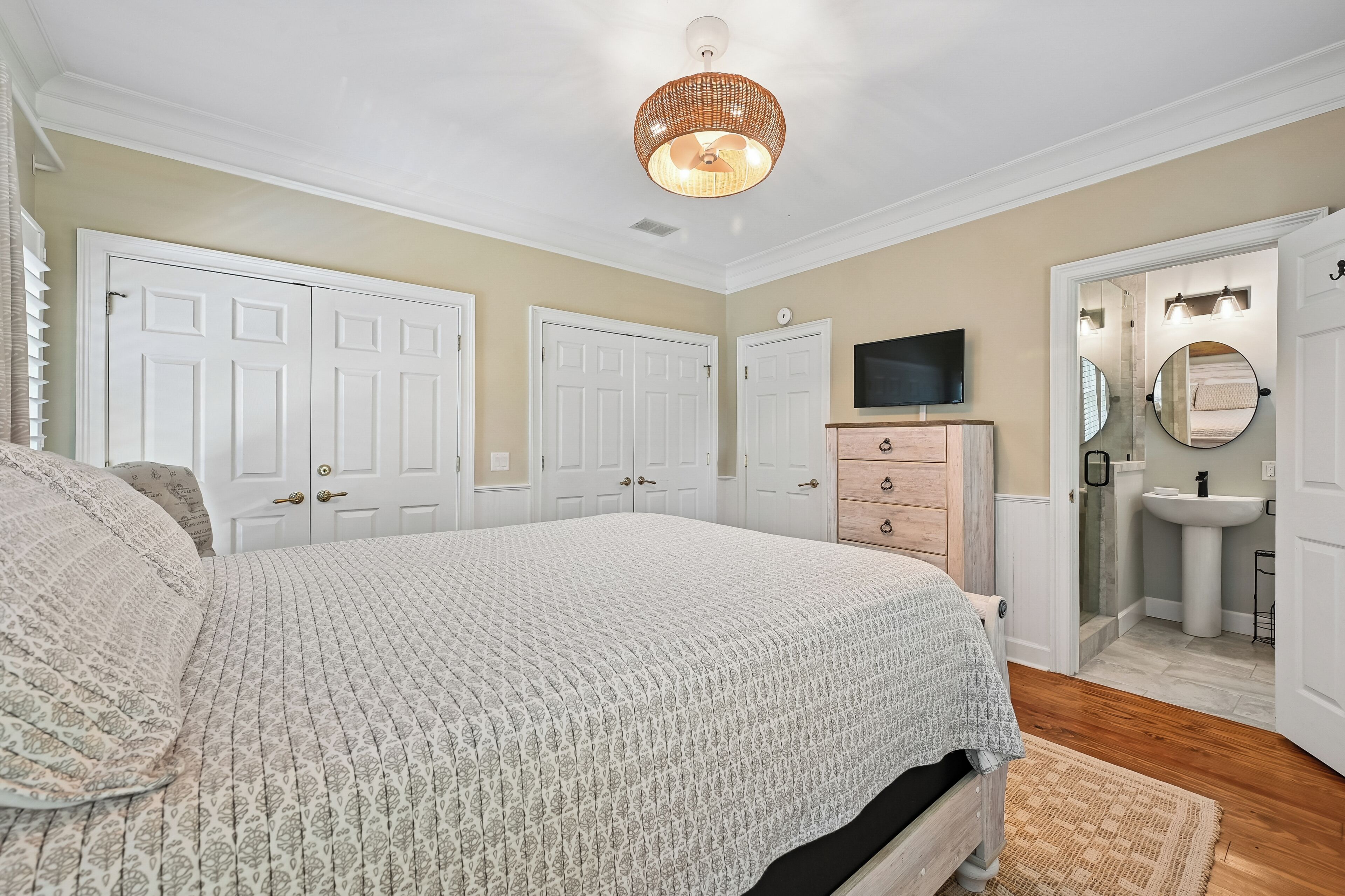 A bedroom with a large bed, a television, a wardrobe, and a bathroom with a sink and mirror.