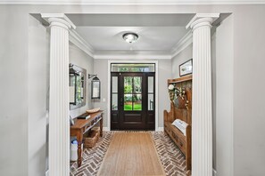 A hallway with a dark wooden door, a white wall with a picture, a wicker basket, a wooden bench, and a rug. - Sea Pines Home w/Views of Harbour Town Golf Course (Hilton Head Island)