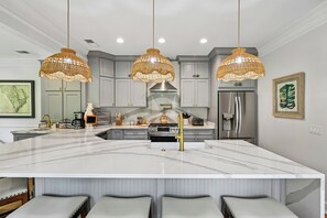 Une cuisine moderne dotée d’un grand îlot central, de meubles gris, d’appareils électroménagers en acier inoxydable et de lustres suspendus en osier.