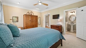 A bedroom with a bed, a wardrobe, a ceiling fan, a television, and a bathroom with a sink and mirror. - Sea Pines Home w/Views of Harbour Town Golf Course (Hilton Head Island)