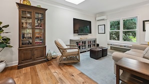 A living room with a wooden cabinet, wicker chair, leather ottoman, and a television on a stand. - Sea Pines Home w/Views of Harbour Town Golf Course (Hilton Head Island)