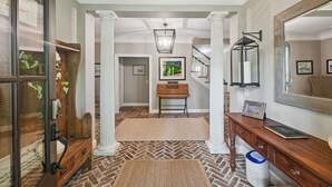 A hallway with a herringbone floor pattern, wooden columns, a desk with a mirror, and a framed picture on the wall. - Sea Pines Home w/Views of Harbour Town Golf Course (Hilton Head Island)