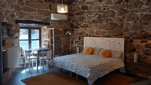 A stone-walled bedroom with a bed, a table, chairs, and a radiator. - 'Casa Agarimo' with Shared Pool, Hot Tub, and Barbecue (Acevedo)