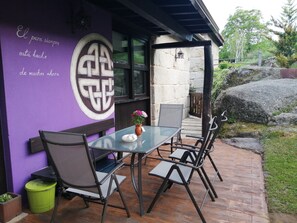 Un patio con un tavolo e sedie in vetro, una parete viola con un simbolo decorativo e un muro in pietra sullo sfondo.