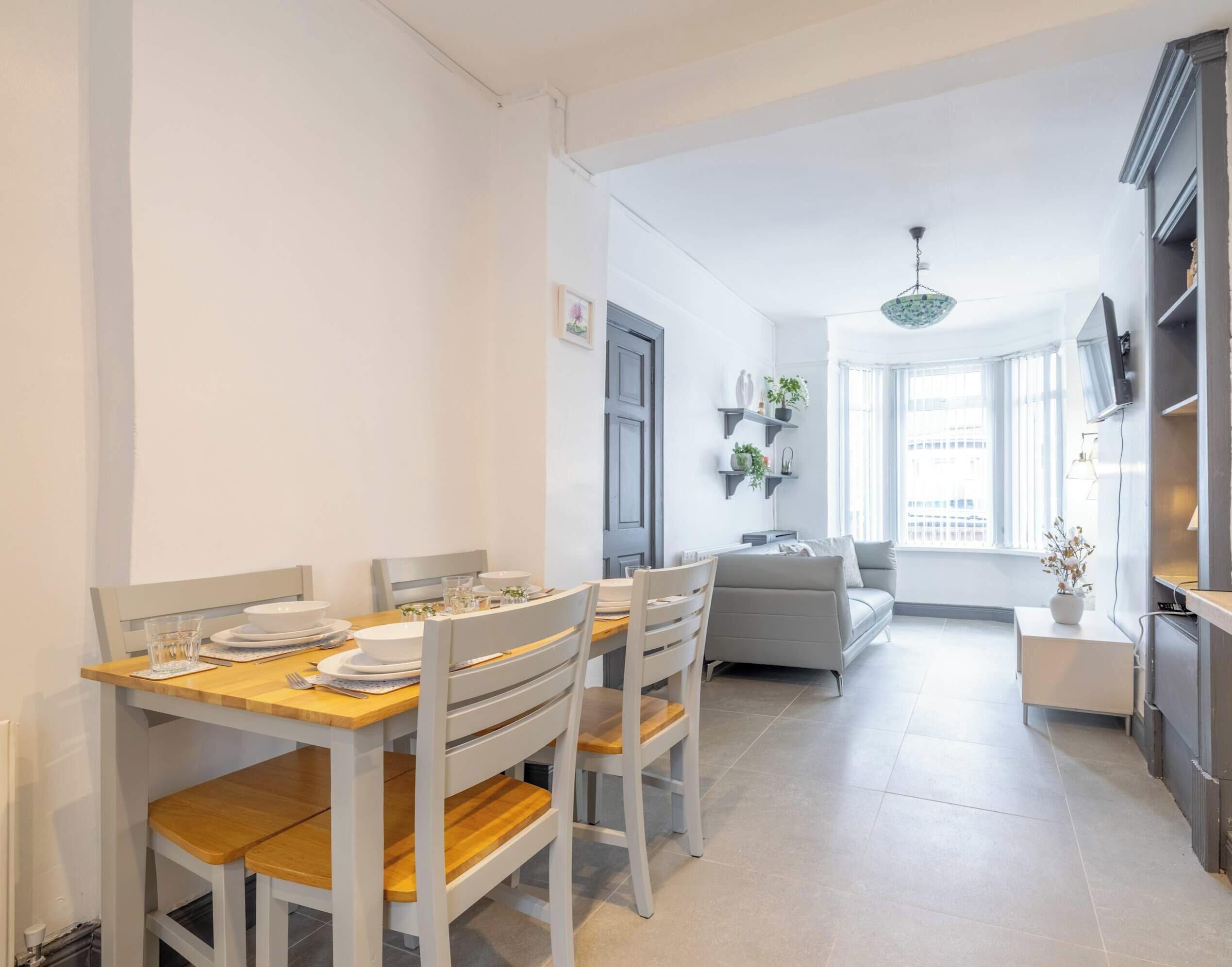 A dining area with a wooden table and chairs, a sofa, a TV, and a window with a city view.