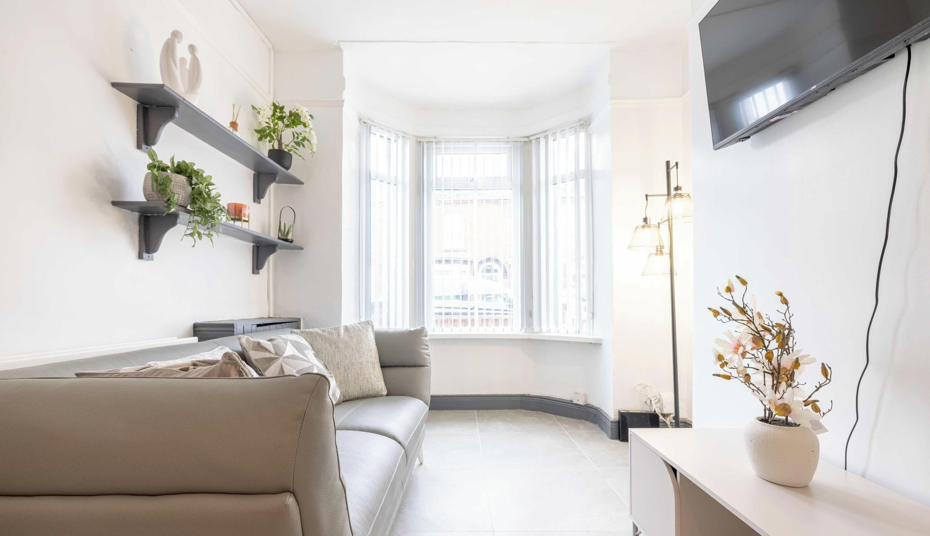 A modern living room with a sofa, a TV mounted on the wall, and a window with a view of buildings.