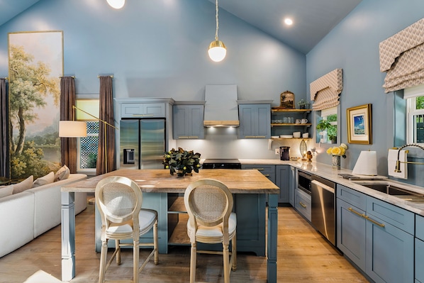 A modern kitchen with a large island, wooden flooring, and blue cabinetry.