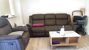 A living room with a brown sofa, a smaller armchair, a wooden coffee table, and a stroller. - Room-spacious Double Room With Garden & (Rathnew)
