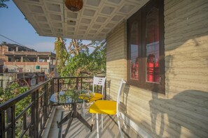 Un balcon avec une table et des chaises, une plante suspendue et une fenêtre avec des volets rouges.