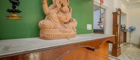 A reception desk with a statue of a deity, a clock, and a fan in a room with green walls.
