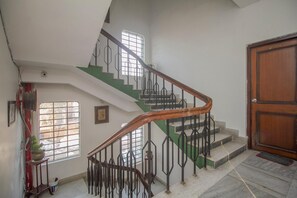 Un escalier avec une main courante en bois et des balustrades en métal, menant à un palier où se trouve une porte portant l’inscription « 204 ».