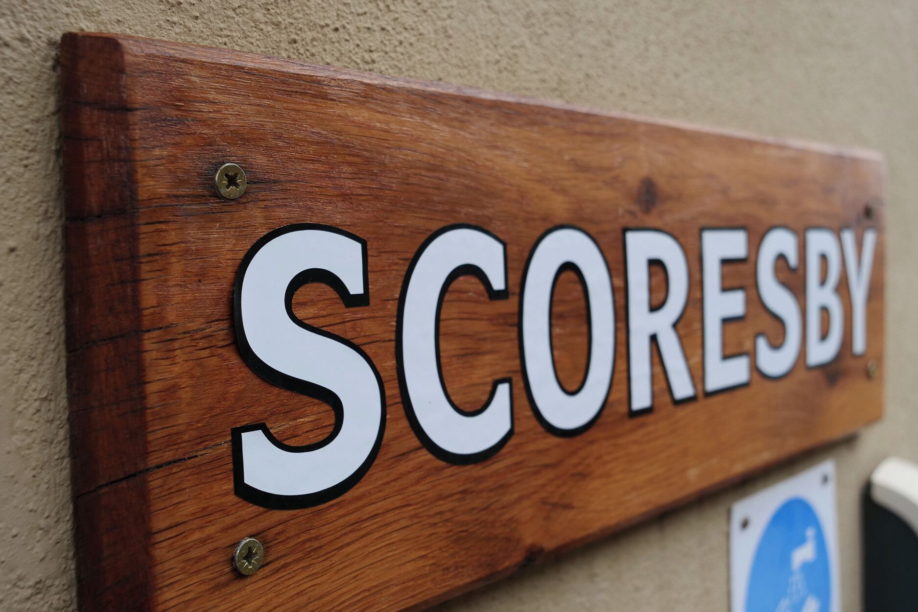 A wooden sign with the word 'SCORESBY' mounted on a wall.