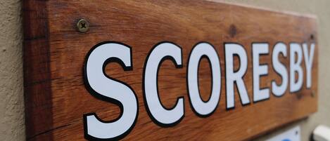 A wooden sign with the word 'SCORESBY' mounted on a wall.