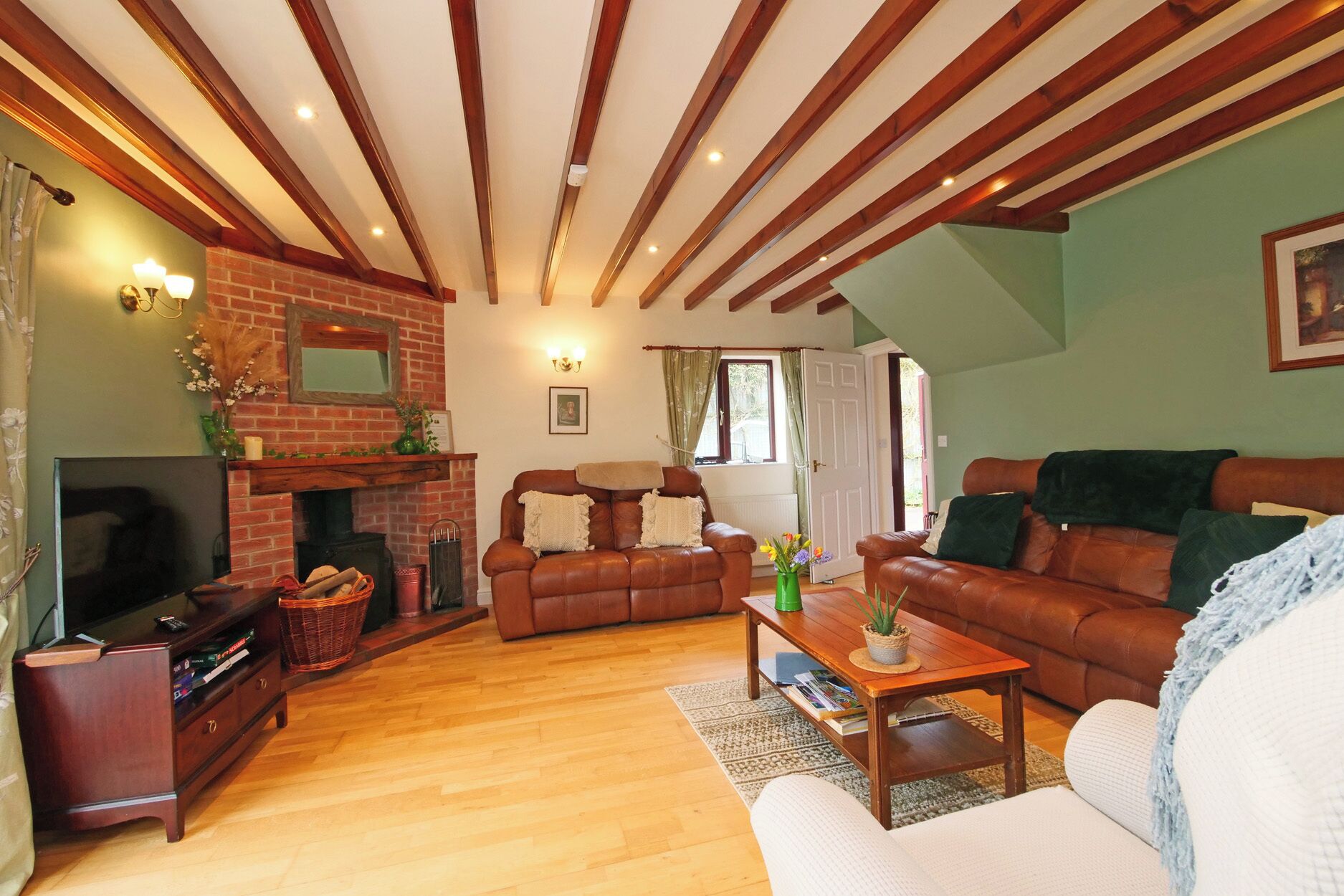 A cozy living room with a fireplace, leather sofas, a television, and a wooden ceiling.
