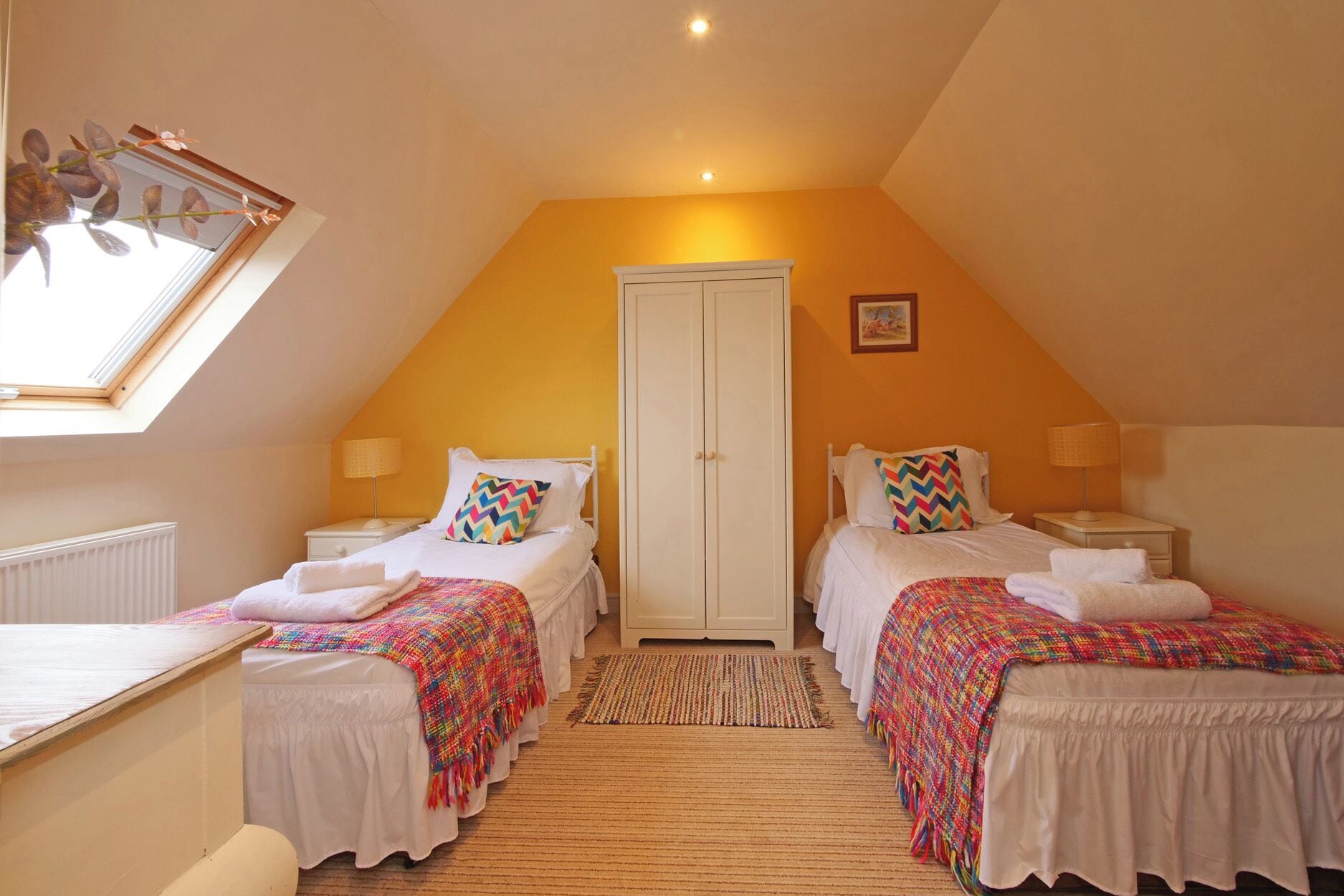 A room with two beds, a white wardrobe, a window with a view, and a ceiling light.