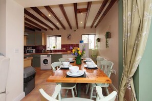 A dining area with a wooden table set for four, surrounded by white chairs. A washing machine is visible in the background. - Scoresby Cottage @ Summerfield Farm (Whitby)