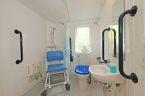 A small bathroom with a wheelchair, a toilet, a sink, and a window. - Abbey View @ Summerfield Farm (Whitby)