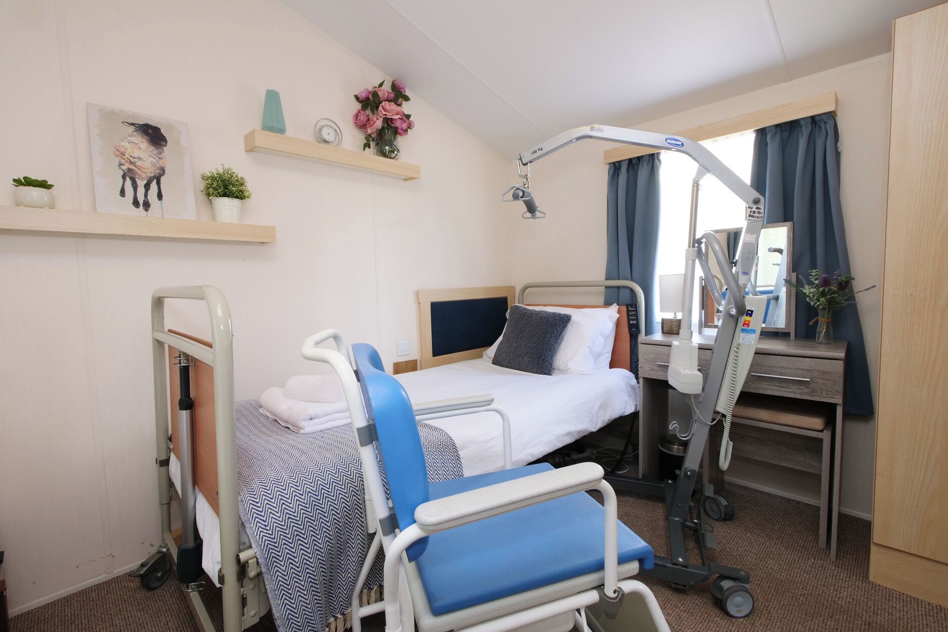 A hospital room with a bed, a bedside table, a chair, a desk, and a window with curtains.