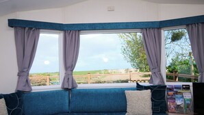 A room with a blue sofa, a window with curtains, and a view of the countryside. - Abbey View @ Summerfield Farm (Whitby)
