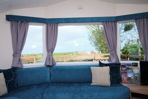 A room with a blue sofa, a window with curtains, and a view of the countryside. - Abbey View @ Summerfield Farm (Whitby)