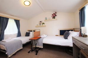 A hotel room with two single beds, a small table, a desk, a chair, a shelf with decorative items, and a window with curtains. - Abbey View @ Summerfield Farm (Whitby)