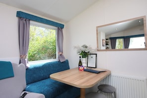 A room with a blue sofa, a wooden table, a mirror, and a window with curtains. - Abbey View @ Summerfield Farm (Whitby)