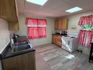 A kitchen with wooden cabinets, a stainless steel sink, a stove, and red and white checkered curtains.